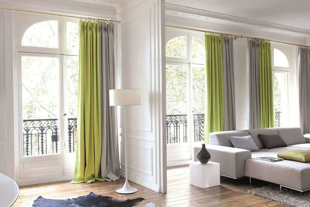 Lime green and grey floor-length curtains on brass poles, framing tall arched balcony doors in a white panelled room