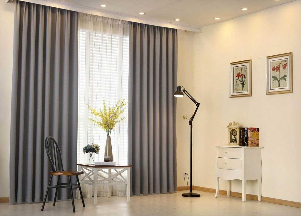 Grey blackout curtains drawn back over a white sheer voile at a tall window, in a cream-walled room