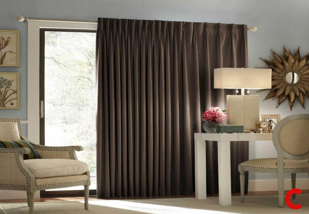 Chocolate brown pinch-pleat curtain pulled to one side of a sliding patio door in a pale blue sitting room
