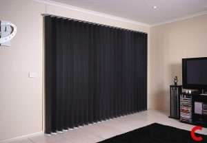 Black vertical blinds closed across a wide lounge window, with a television and tiled floor to one side