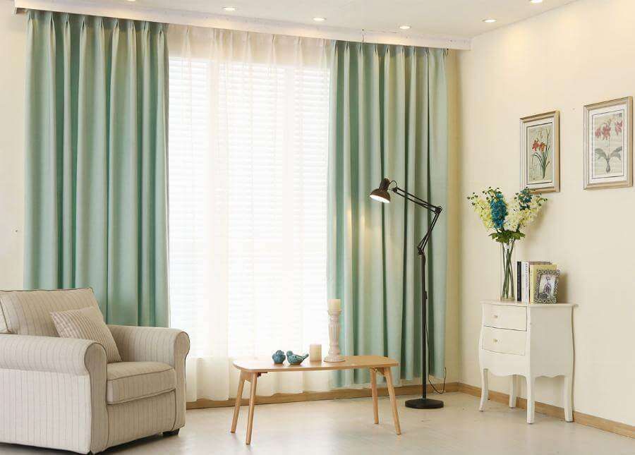 Mint green blockout curtains layered over a white sheer beside a striped armchair