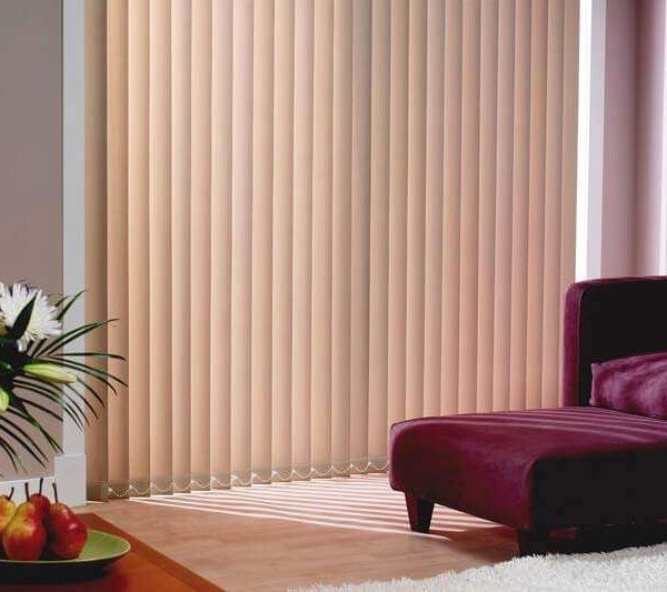 Peach vertical blinds closed across a floor-to-ceiling window beside a burgundy velvet chaise longue