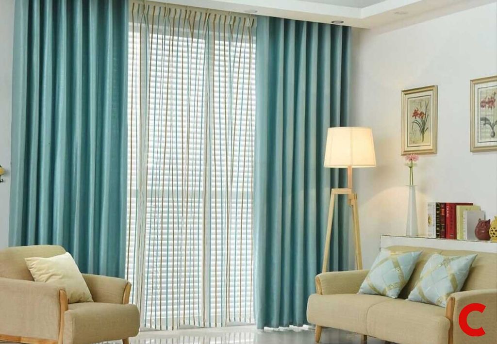 Teal curtains parted over a striped sheer at a full-height balcony door, with beige sofa and tripod lamp