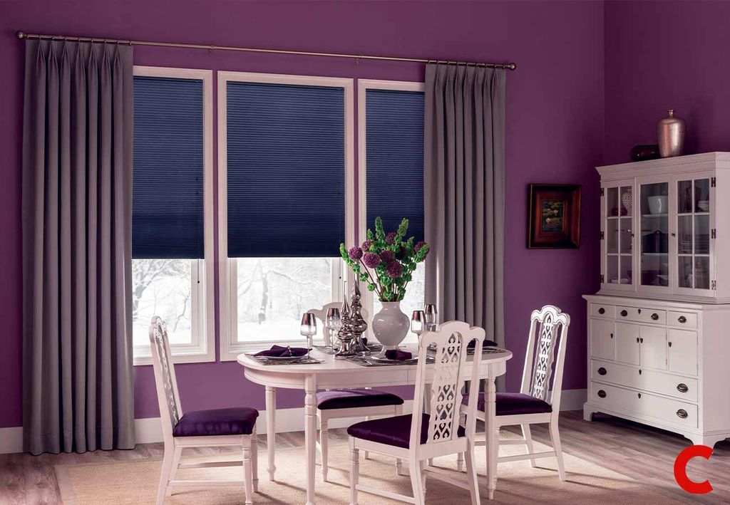 Grey curtains on a brass pole beside navy pleated blinds half lowered over a dining room window, purple walls