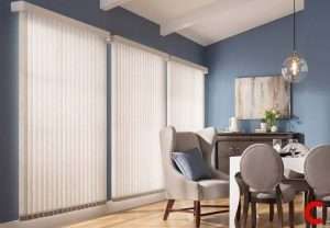 Ivory vertical blinds on three tall windows in a blue dining room with a grey wingback chair