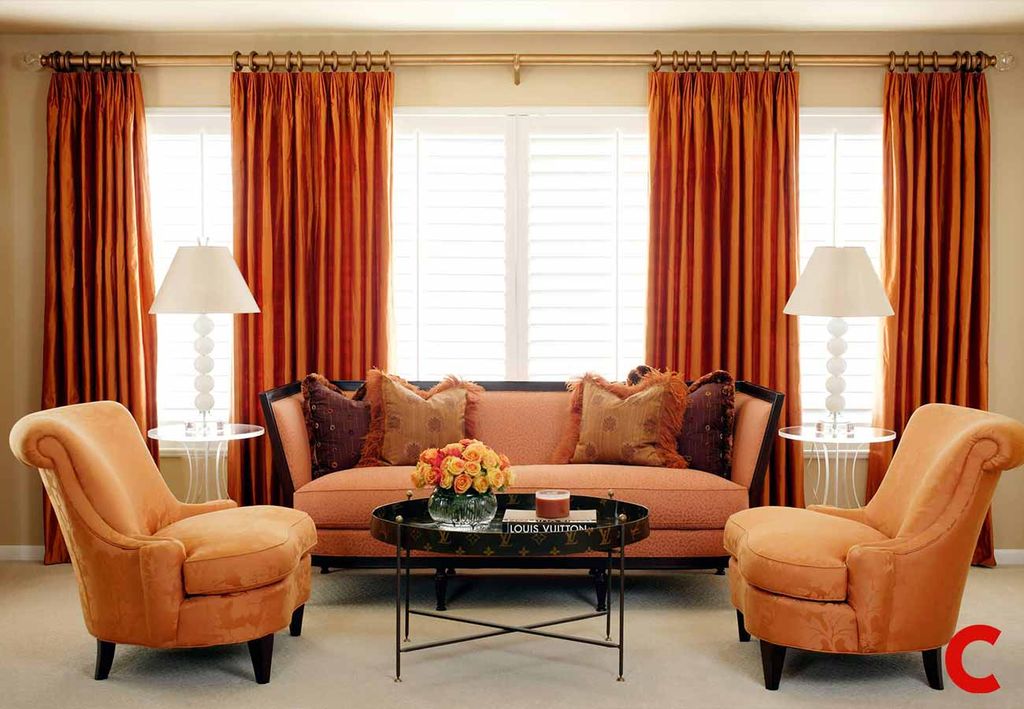 Burnt orange silk curtains on a brass pole over white plantation shutters, framing a coral sofa