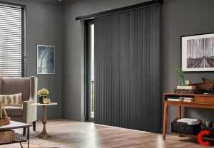 Charcoal vertical blinds drawn across a sliding door, stacked open at one edge, beside a wooden console