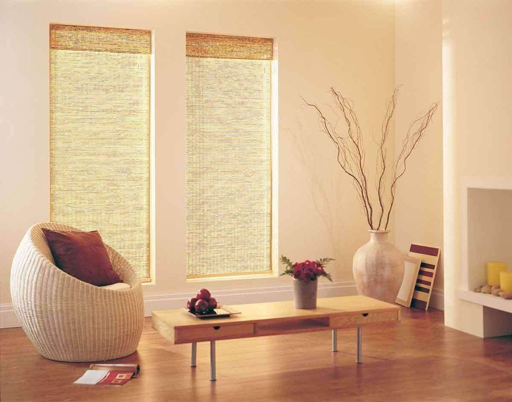 Natural woven bamboo shades lowered over two tall windows, sunlight glowing through the reeds beside a wicker chair