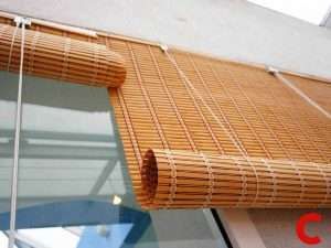 Golden bamboo roll-up blind viewed from below on a balcony, partly rolled at the bottom rail