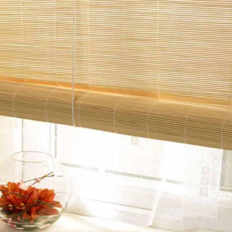Straw-coloured bamboo roll-up blind raised high over a bright window, orange flowers in a glass bowl below