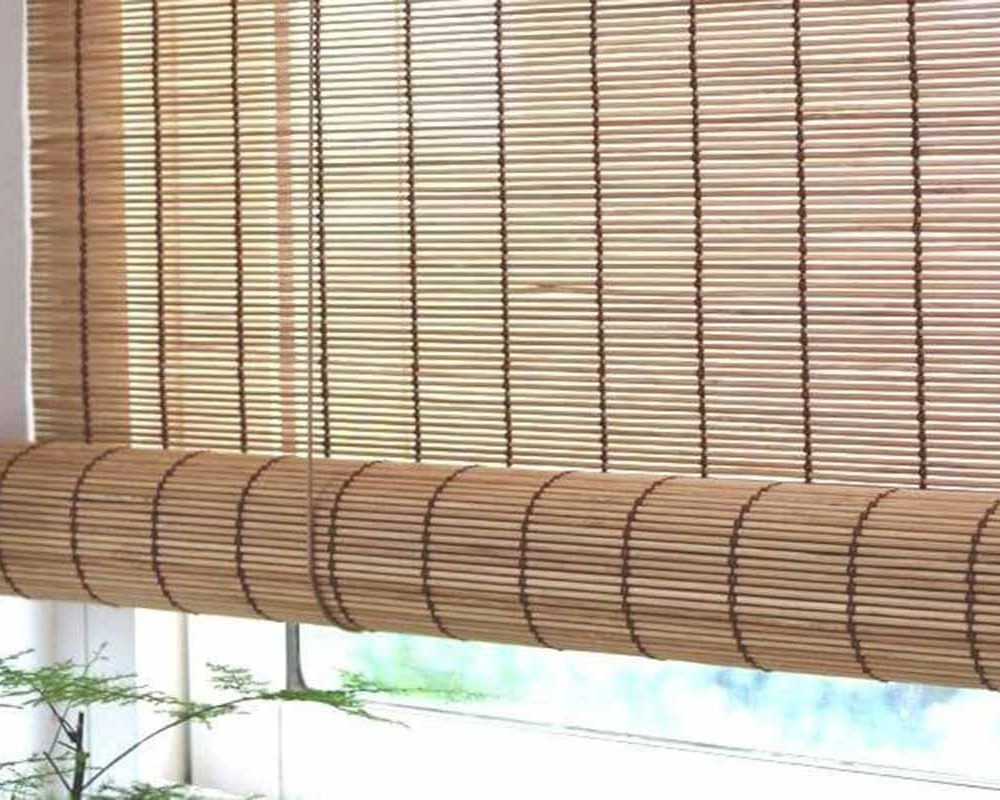 Mid-brown bamboo roll-up blind lowered most of the way, its rolled bundle across a sunlit window