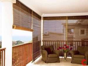 Dark brown bamboo roll-up blinds shading a covered balcony with a timber rail and two armchairs