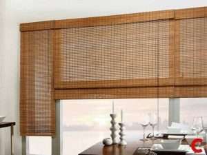 Woven bamboo blinds with a matching pelmet wrapping a corner window above a dark dining table