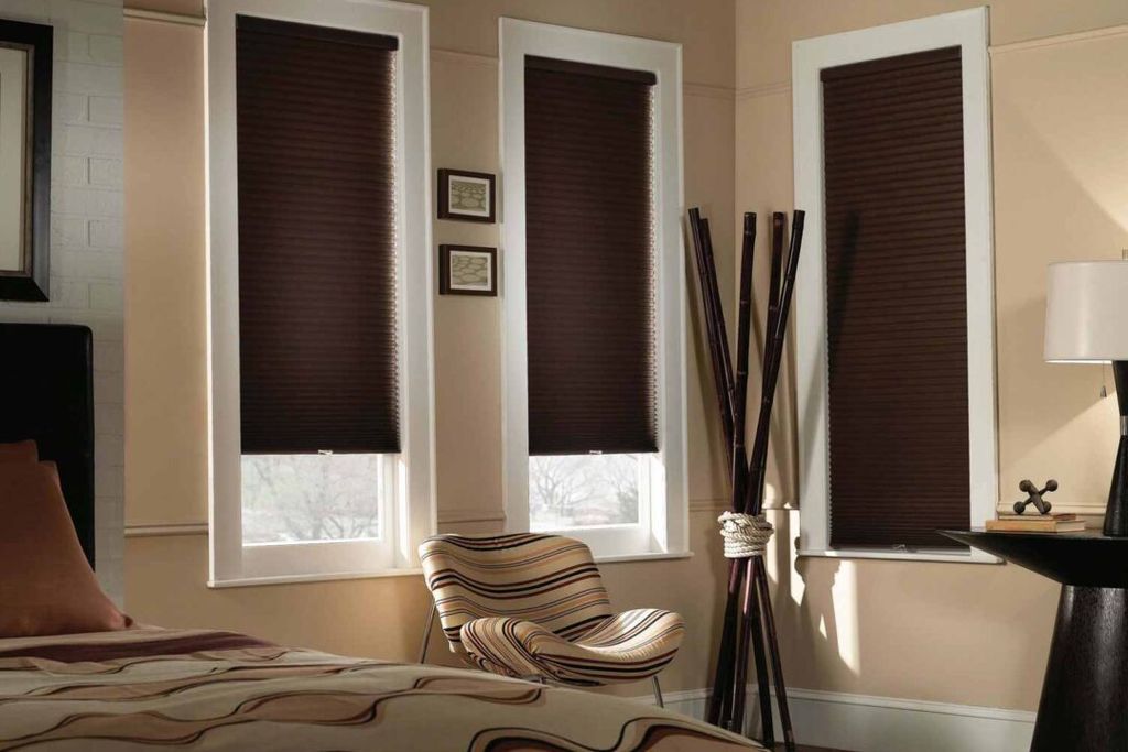 Dark brown pleated blinds lowered halfway down three tall bedroom windows with white painted surrounds
