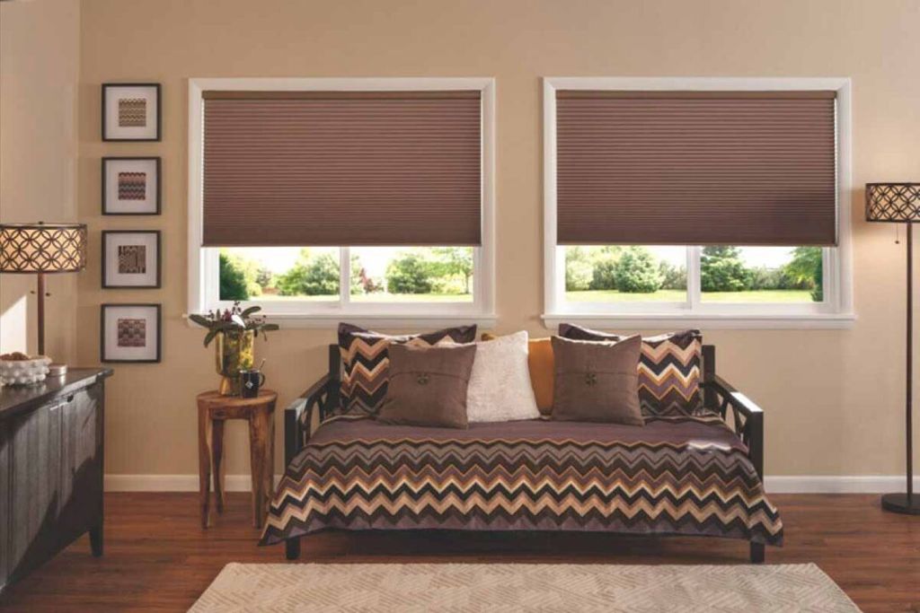 Brown honeycomb cellular blinds lowered two-thirds over a pair of windows above a chevron-covered daybed