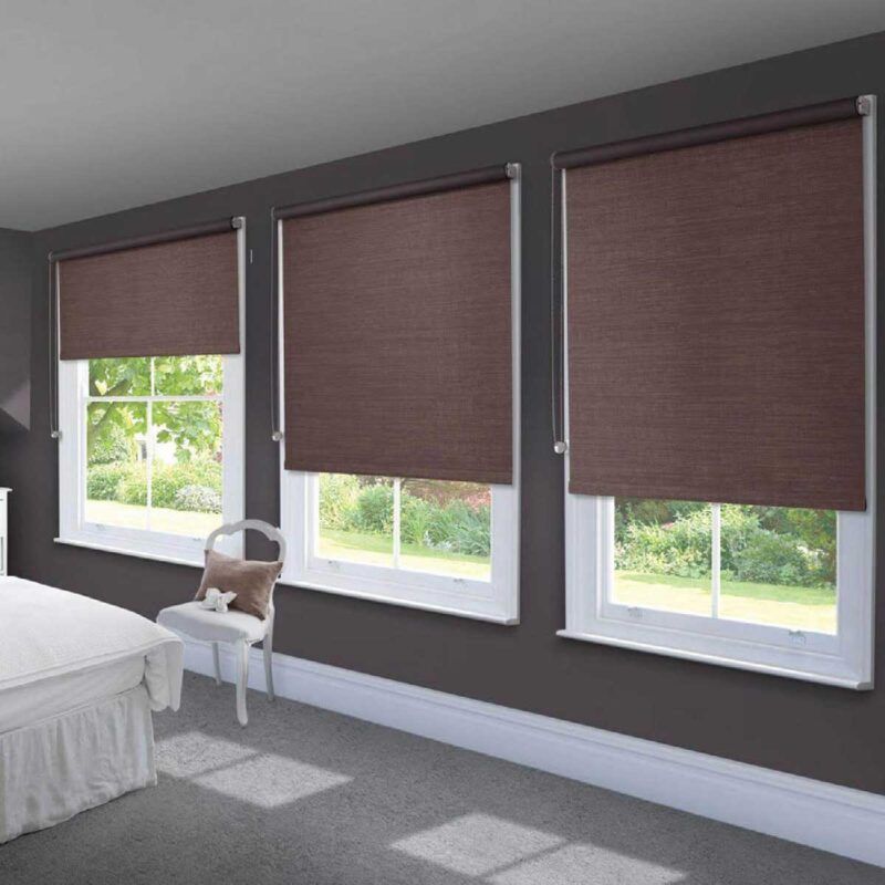 Three burgundy textured roller blinds part lowered over sash windows in a bedroom with dark aubergine walls