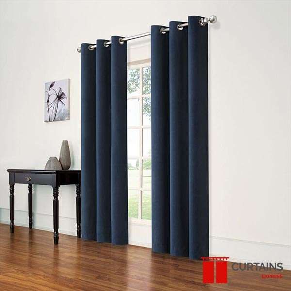 Navy eyelet curtain panels on a chrome pole drawn part-way across a garden window above a dark wood floor