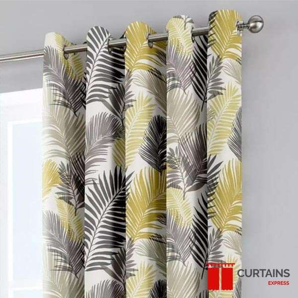 Close-up of cream eyelet curtains printed with grey and yellow palm leaves, hung on a steel pole