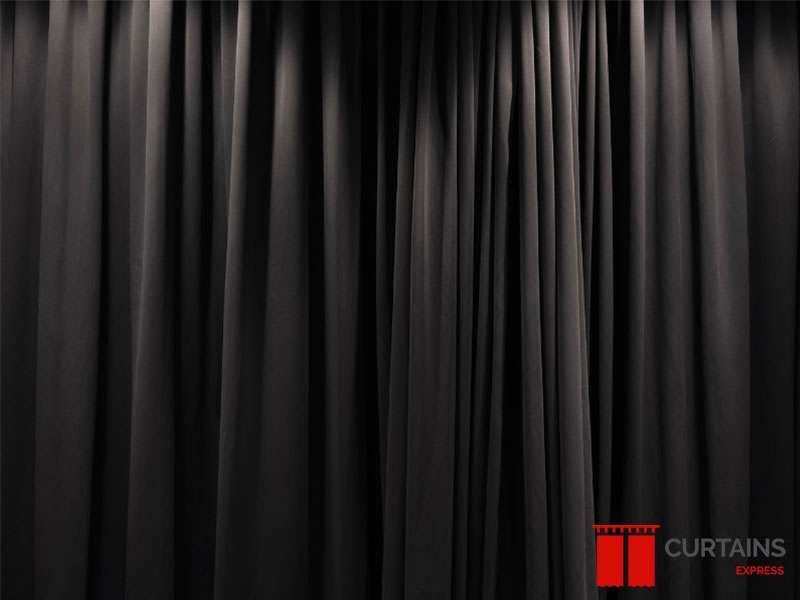 Densely gathered black curtain fabric filling the frame, lit from above so the folds read as ridges