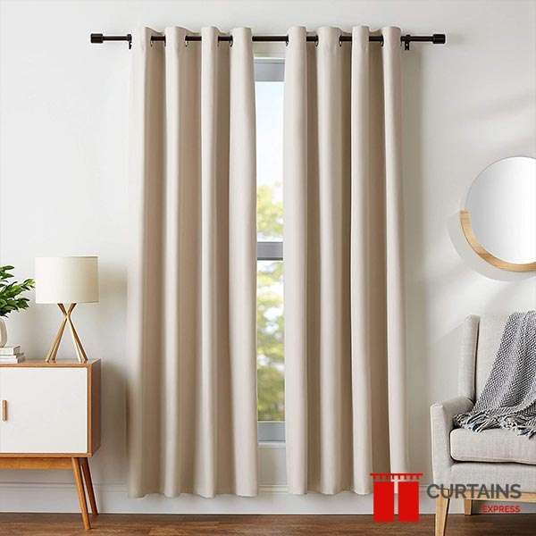 Cream eyelet curtains on a slim black pole, hung sill-length at a narrow window beside a wooden sideboard