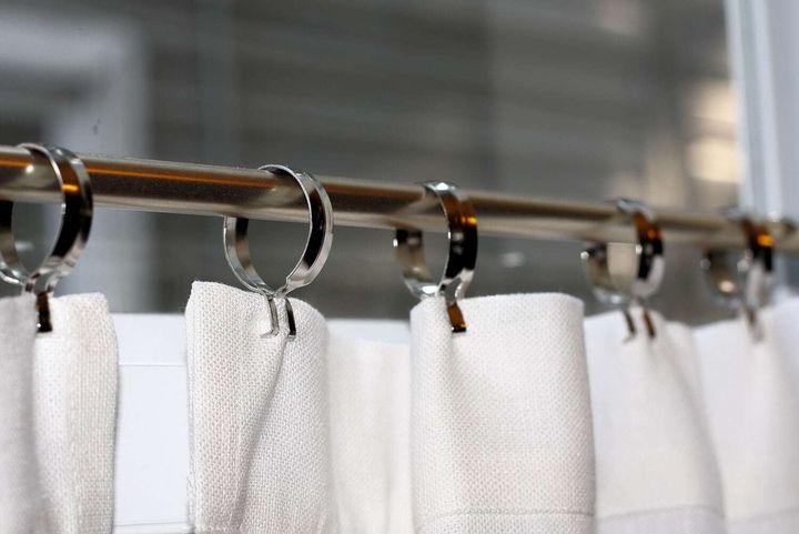Nickel curtain rings on a metal rod holding a white cotton-weave heading