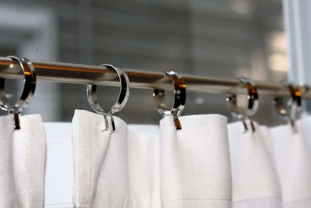 Close-up of chrome curtain rings on a polished metal pole, carrying the pleated heading of a white curtain