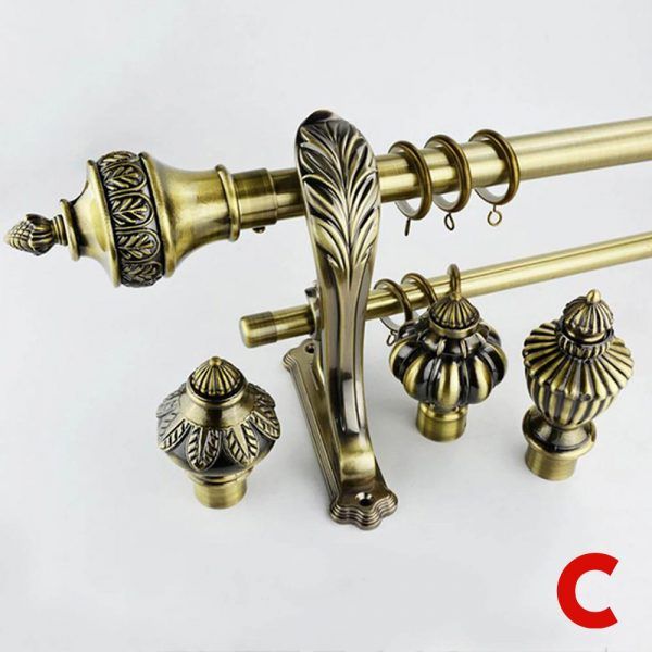 Antique brass curtain poles, ornate finials, rings and a wall bracket arranged on a plain white background