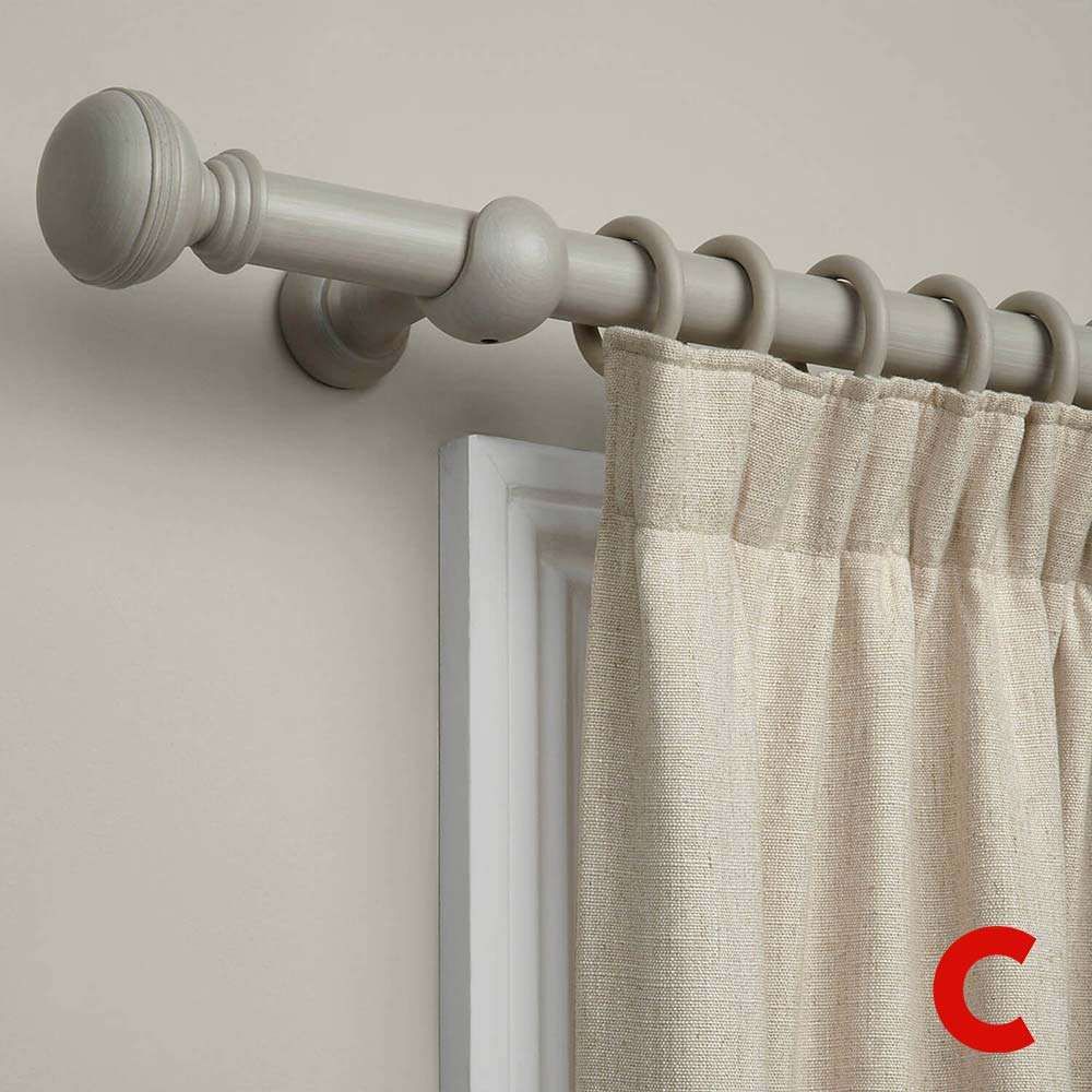 Pale grey wooden curtain pole with a ball finial and matching rings carrying a cream linen curtain above a door frame