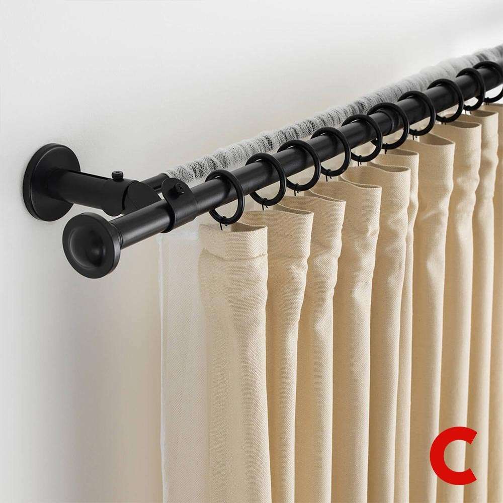 Black wall-bracketed pole with rings holding cream pinch-pleat curtains layered over a grey sheer behind
