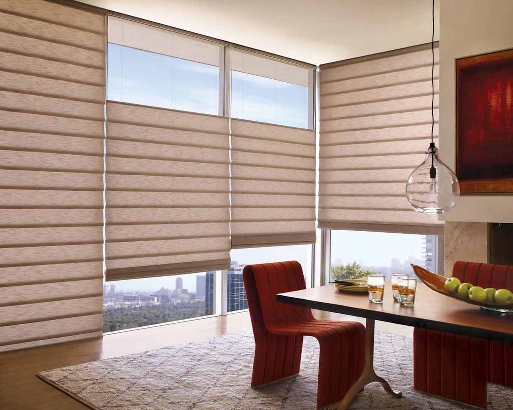 Oatmeal soft-fold roman blinds part-raised across corner windows in a dining room, city skyline beyond