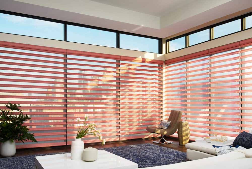 Coral sheer horizontal shades wrapping corner floor-to-ceiling windows, sunlight casting banded shadows on the floor