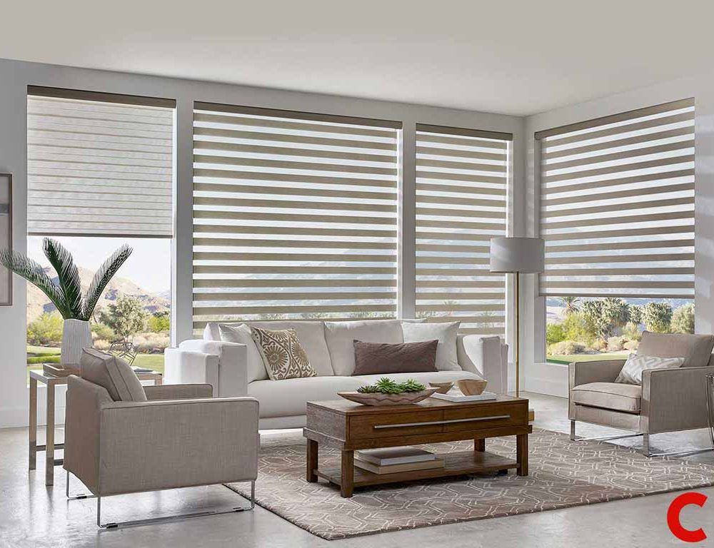 Taupe and white striped zebra blinds fitted to five windows of a desert-view living room with grey armchairs