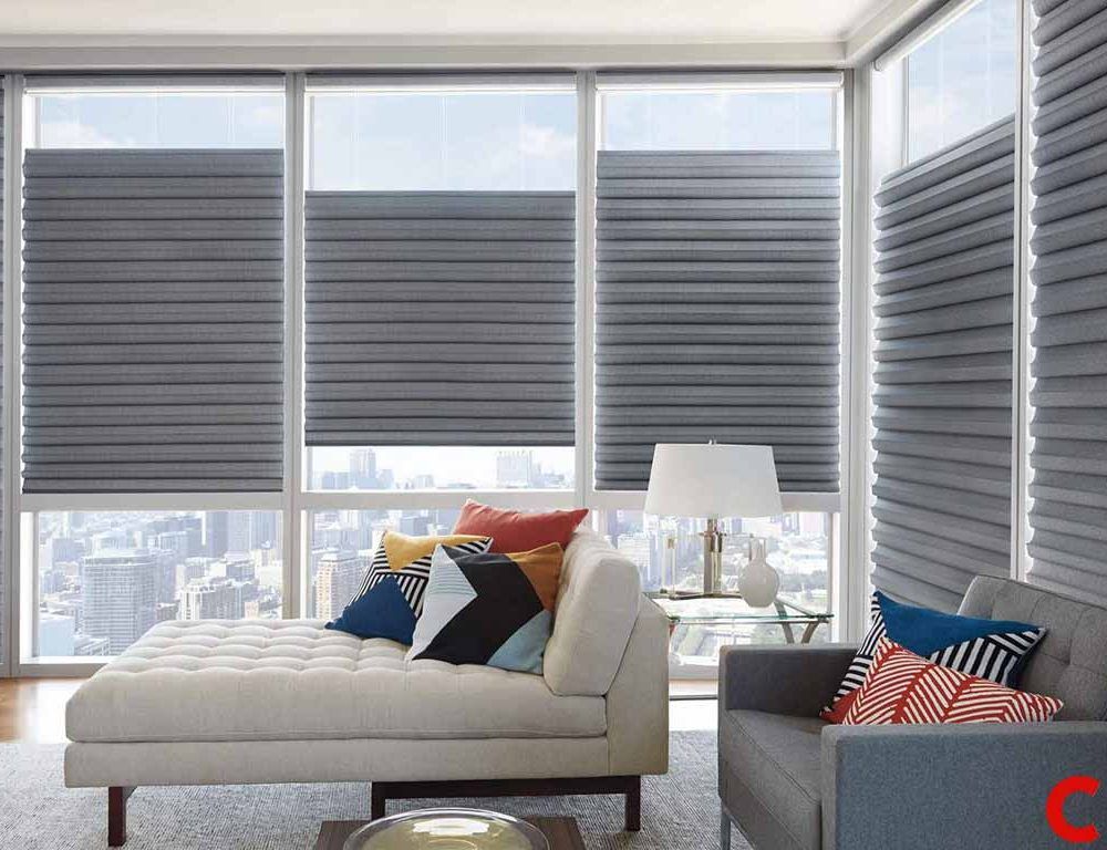 Charcoal roman shades half lowered on corner floor-to-ceiling windows of an apartment high above a city skyline