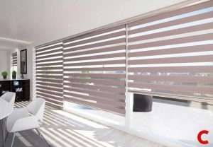 Grey zebra blinds along a glazed wall of a dining area, throwing striped shadows across a pale tiled floor