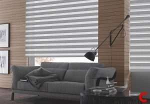 White zebra blind filling a window behind a grey sofa, with a black angled floor lamp and wood-panelled wall