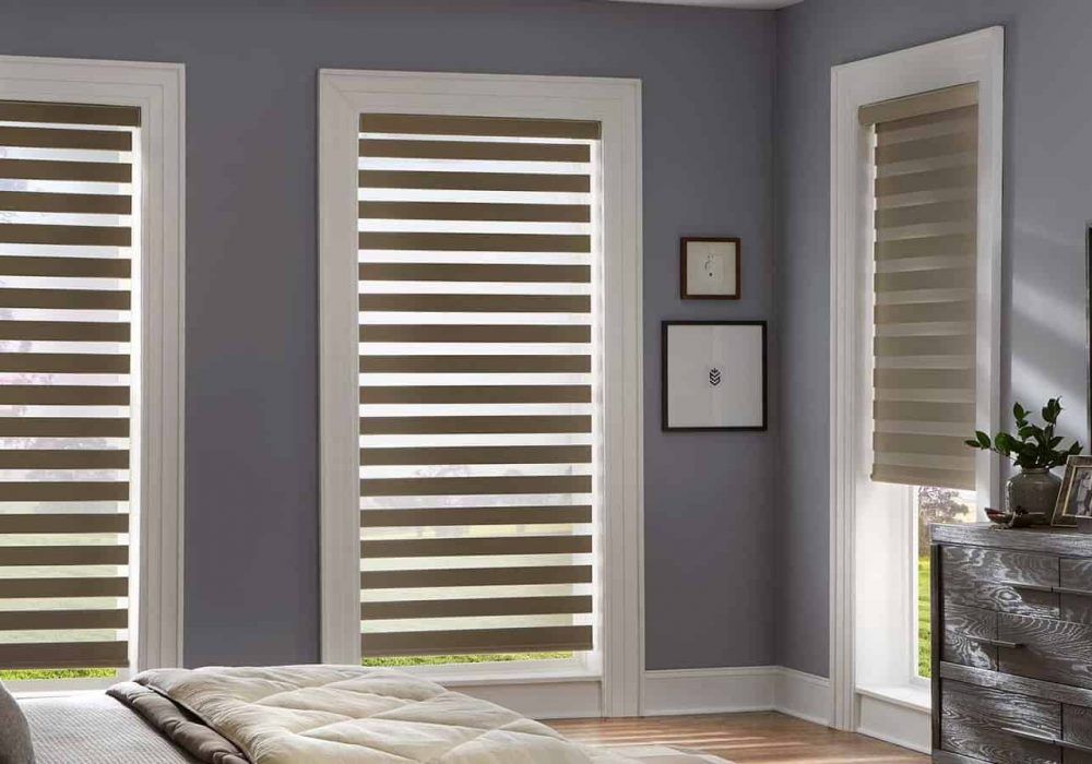 Olive zebra blinds in three white-framed bedroom windows against slate grey walls, bed in the foreground
