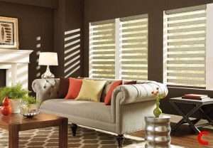 Cream zebra blinds on windows either side of a fireplace in a brown-walled sitting room with a buttoned sofa