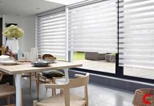 White zebra blinds covering sliding glass doors in an open-plan kitchen-diner looking onto a paved terrace