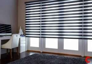 Navy and white zebra blinds spanning a wide window above a home-office desk, shaggy grey rug below