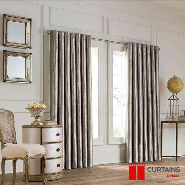 Silver-grey eyelet curtains on a slim pole hanging in deep even folds against a white-panelled wall