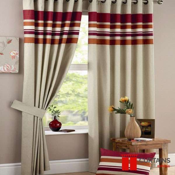 Natural linen eyelet curtains with a red and orange striped top border, one panel gathered in a fabric tieback