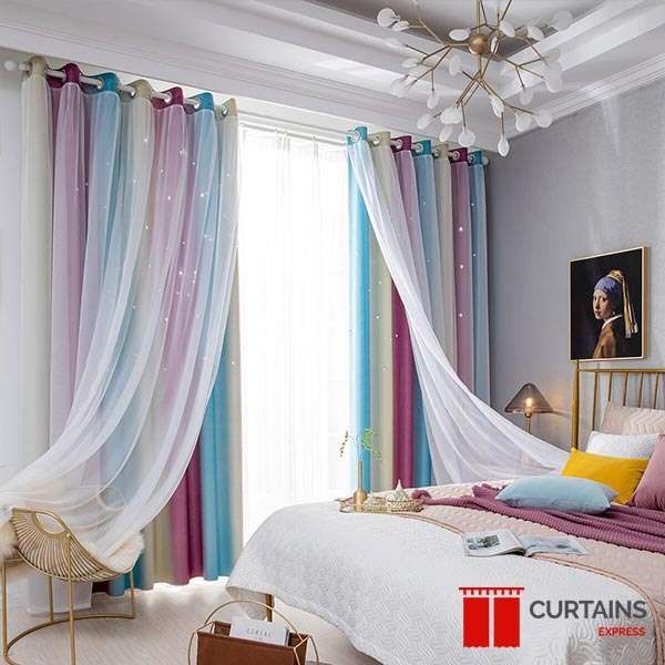Pink and blue ombre eyelet curtains under a star-cut white sheer, swept across a bedroom window