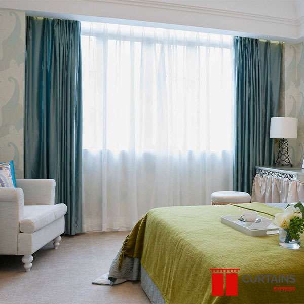 Teal curtains drawn back over a full white sheer at a wide bedroom window, lime green bedspread below