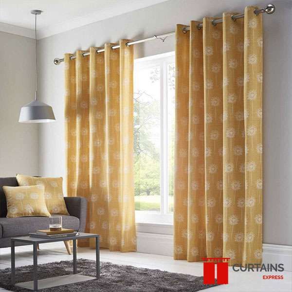 Mustard eyelet curtains printed with white dandelion heads, framing a window in a grey living room
