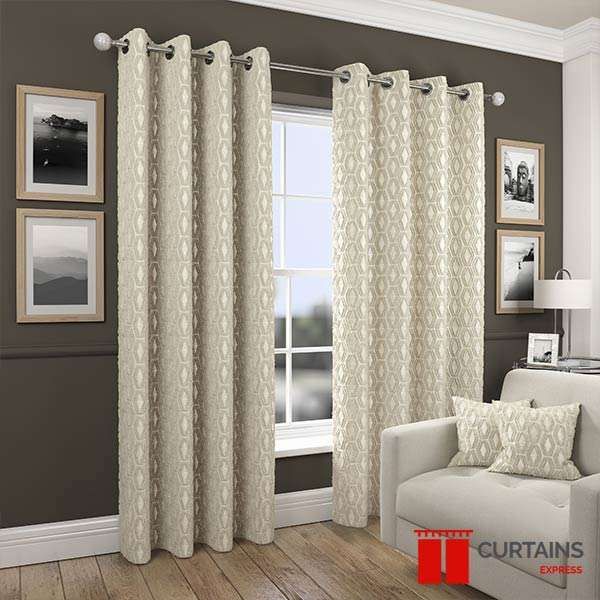 Cream eyelet curtains woven with a raised hexagon trellis, hung against a dark taupe wall by a small window