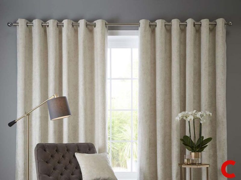 Cream chenille eyelet curtains on a chrome pole either side of a white-framed window, brown buttoned chaise below