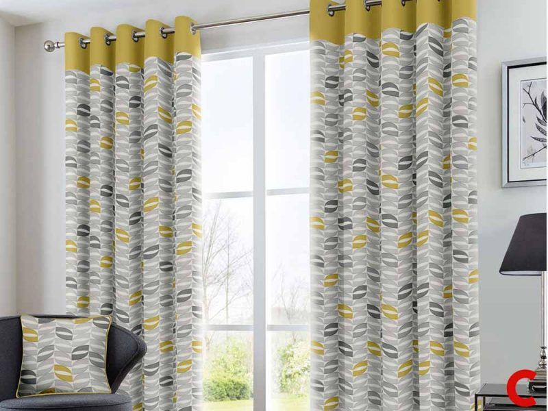 Grey and mustard leaf-print eyelet curtains with a plain yellow top band, open across patio doors to a garden