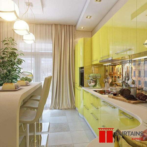 Champagne floor-length curtain tied back beside a white sheer at a balcony door in a yellow gloss galley kitchen