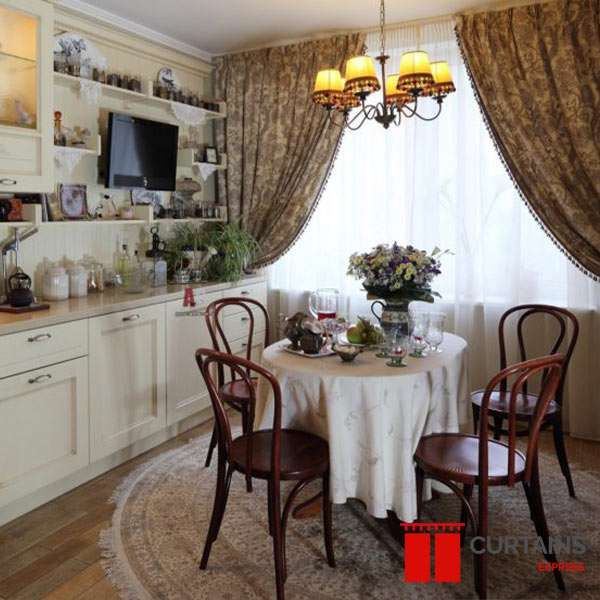 Gold-brown damask curtains with tasselled trim swept back over a white sheer above a round dining table