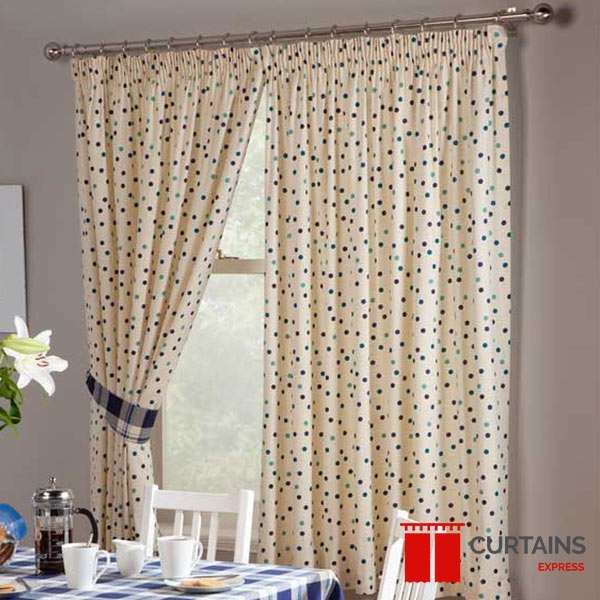 Cream pencil-pleat curtains printed with multicoloured polka dots on a chrome pole, one panel held by a check tieback